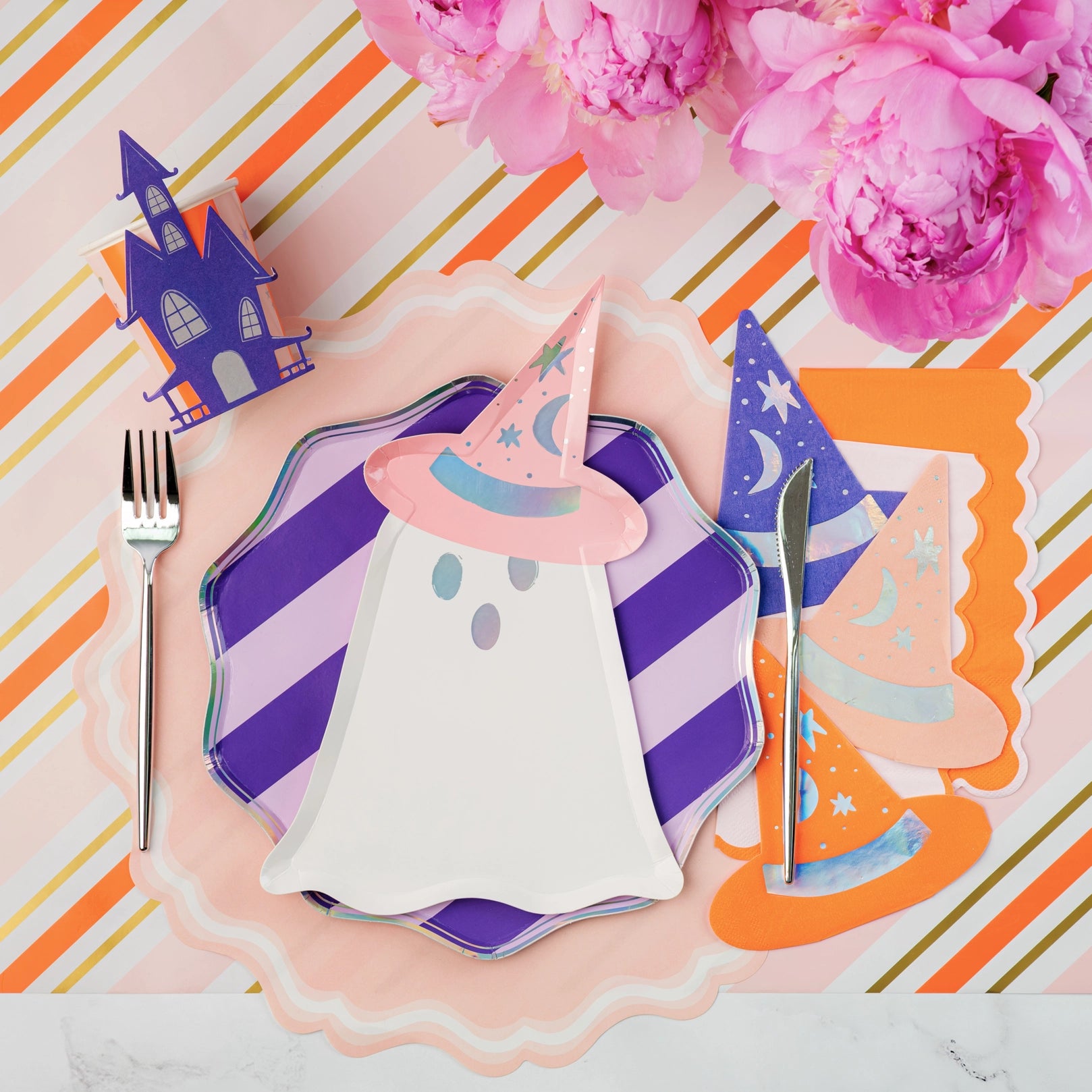 Halloween-themed place setting with ghost, witch hat, and candy house on a colorful striped background.