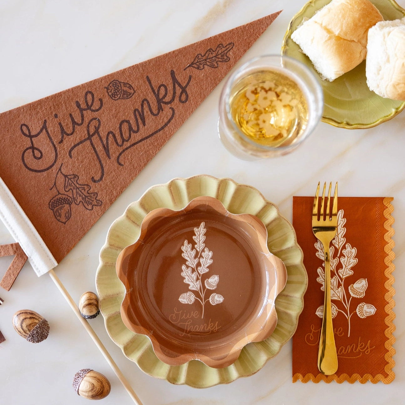 Decorative table setting with a 'Give Thanks' pennant, ceramic dish, and bread on a marble surface.